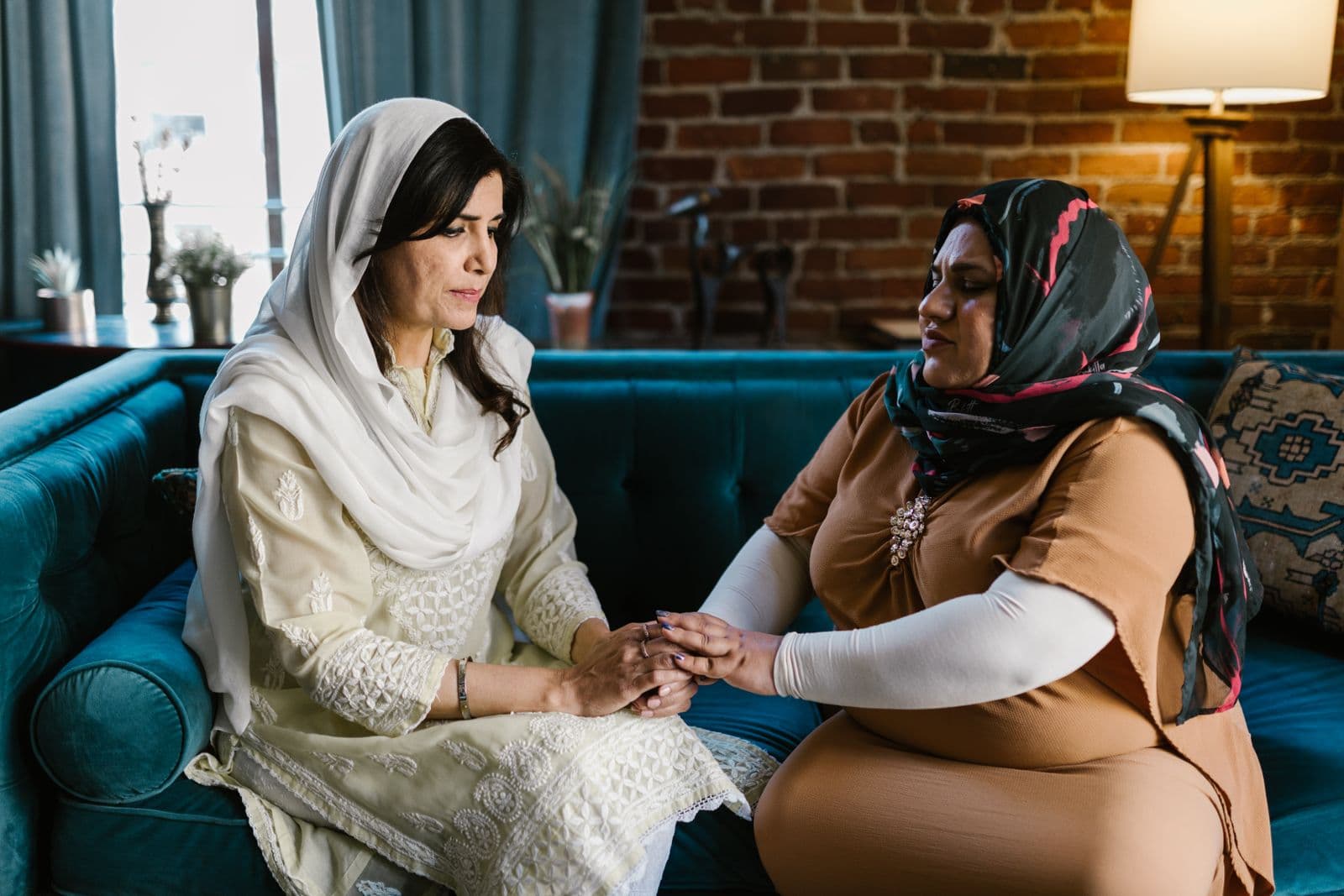 Two women sitting together on a sofa, one holding the other’s hands in support